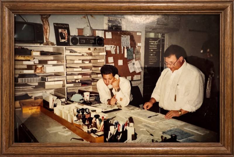 Framed photograph, two generations working at the shop counter